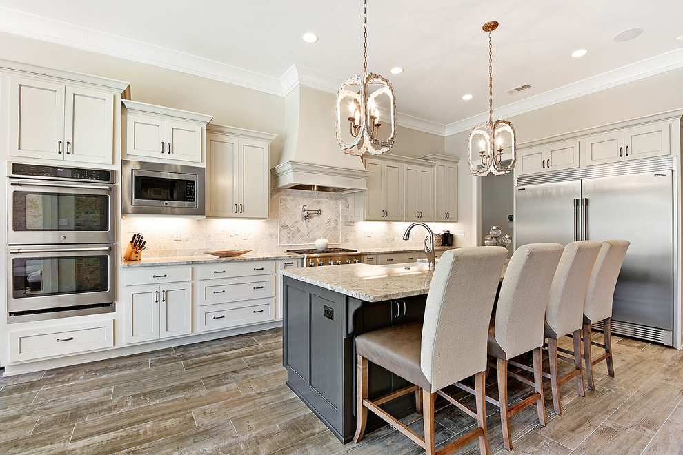 Example of a large transitional l-shaped porcelain tile and brown floor open concept kitchen design in New Orleans with a farmhouse sink, beaded inset cabinets, white cabinets, granite countertops, gray backsplash, marble backsplash, stainless steel appliances and an island