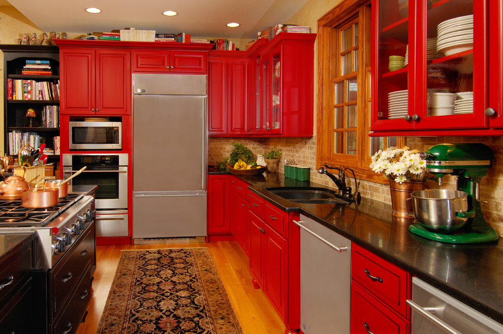 Cette photo montre une cuisine montagne avec un placard à porte vitrée, des portes de placard rouges, un plan de travail en granite, une crédence beige et îlot.