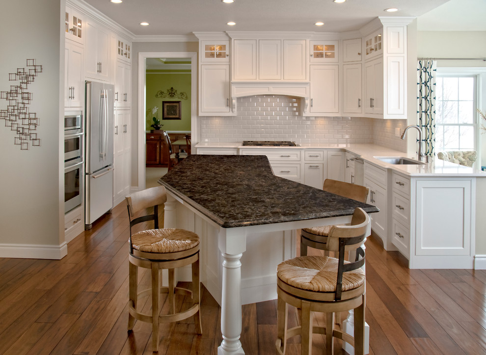 Klassisk inredning av ett mellanstort kök, med en undermonterad diskho, skåp i shakerstil, vita skåp, vitt stänkskydd, stänkskydd i tunnelbanekakel, rostfria vitvaror, mellanmörkt trägolv, en köksö, granitbänkskiva och brunt golv