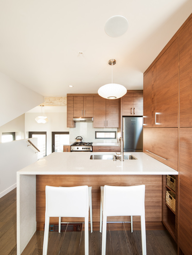 Exempel på ett litet modernt kök, med släta luckor, skåp i mellenmörkt trä, bänkskiva i kvarts, vitt stänkskydd, rostfria vitvaror, en halv köksö, en dubbel diskho, mellanmörkt trägolv och grått golv