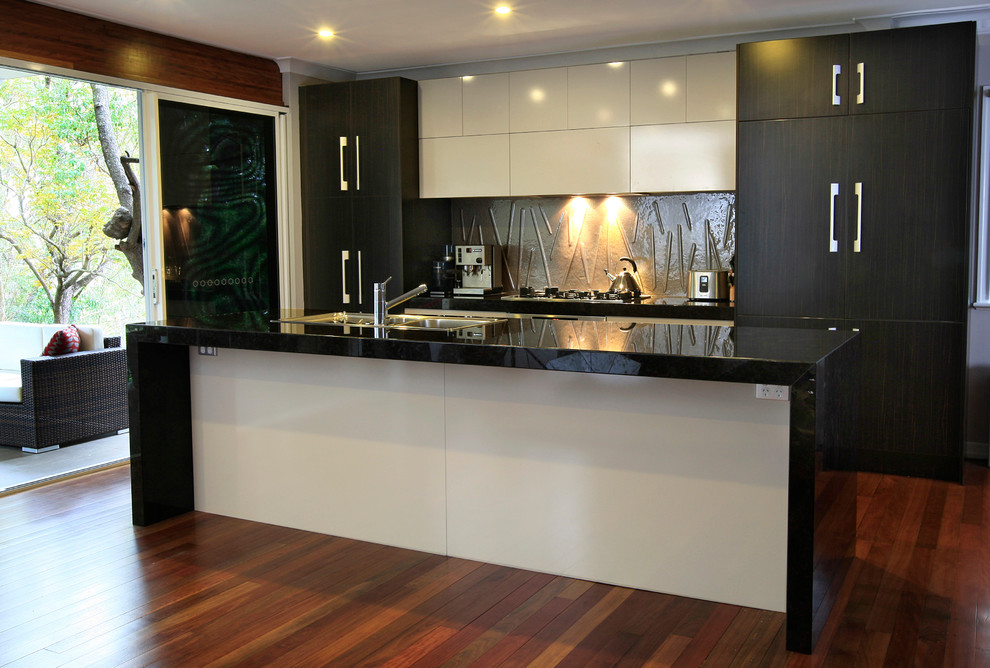 Zweizeilige, Mittelgroße Moderne Wohnküche mit Doppelwaschbecken, flächenbündigen Schrankfronten, dunklen Holzschränken, Granit-Arbeitsplatte, Küchenrückwand in Beige, Glasrückwand, Küchengeräten aus Edelstahl, hellem Holzboden und Kücheninsel in Brisbane