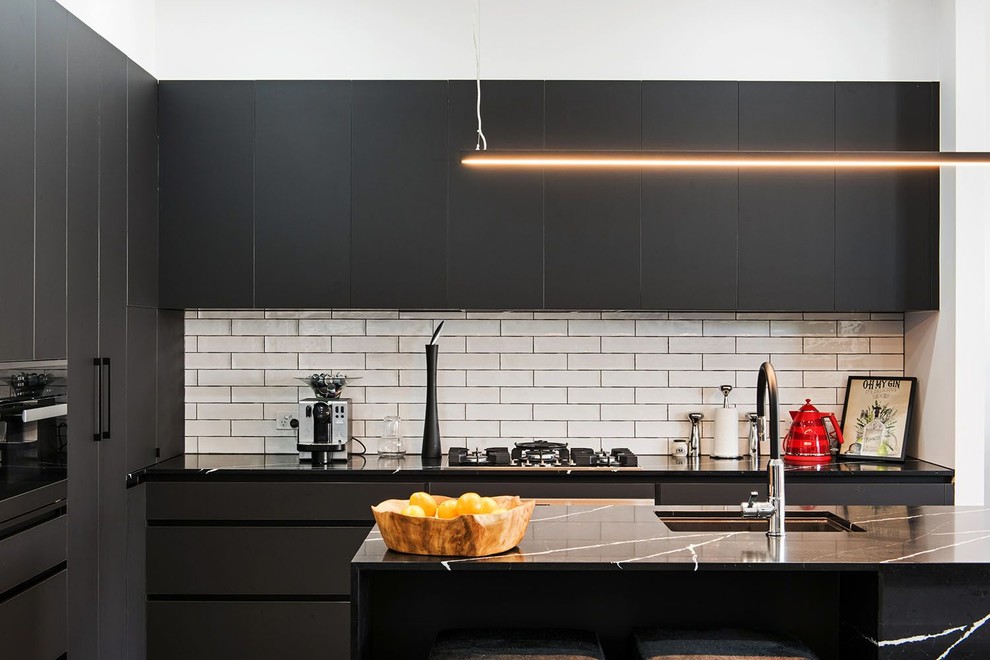Idéer för ett mellanstort modernt svart kök, med en nedsänkt diskho, svarta skåp, marmorbänkskiva, vitt stänkskydd, stänkskydd i tunnelbanekakel, svarta vitvaror och en köksö