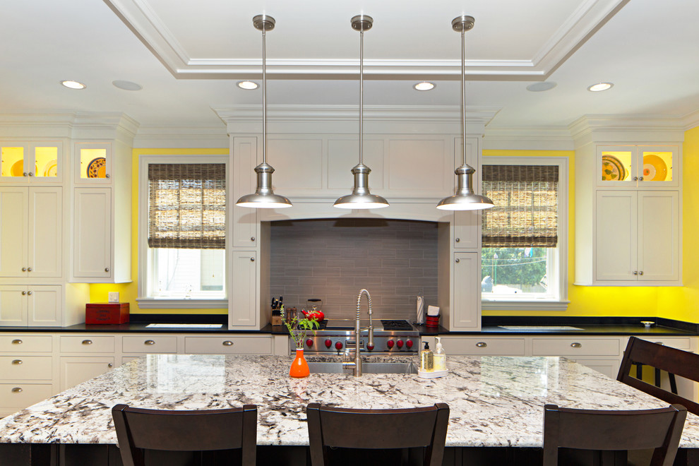 Example of a large classic l-shaped travertine floor eat-in kitchen design in Chicago with an undermount sink, recessed-panel cabinets, white cabinets, granite countertops, gray backsplash, stainless steel appliances and an island