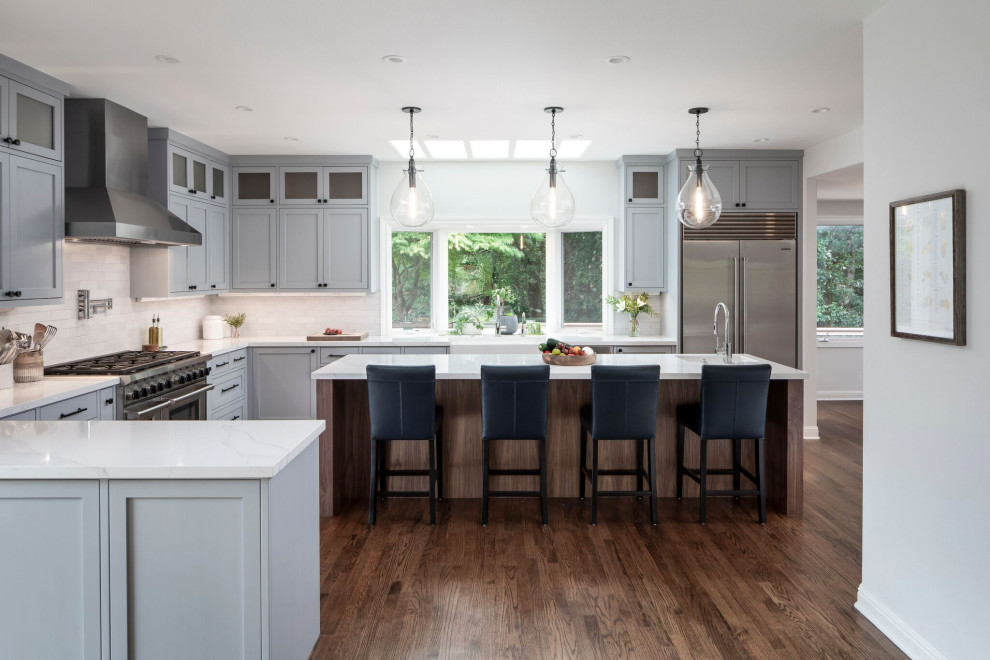 Example of a large transitional u-shaped medium tone wood floor and brown floor open concept kitchen design in Other with a farmhouse sink, shaker cabinets, gray cabinets, quartz countertops, white backsplash, brick backsplash, stainless steel appliances, an island and white countertops