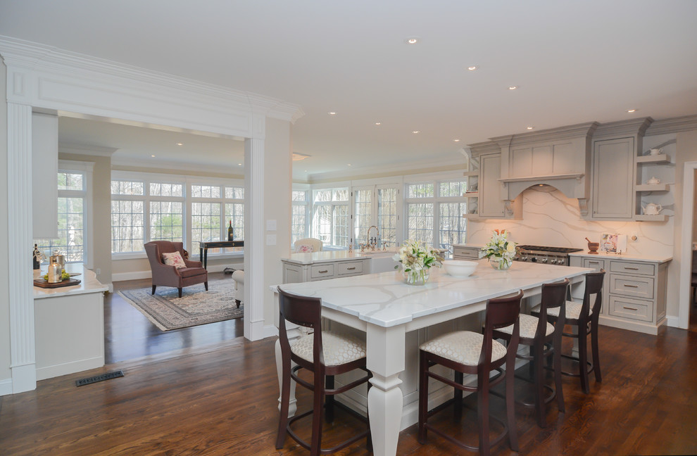 Example of a huge classic u-shaped medium tone wood floor open concept kitchen design in Boston with a farmhouse sink, beaded inset cabinets, gray cabinets, quartz countertops, white backsplash, stone slab backsplash, stainless steel appliances, two islands and white countertops