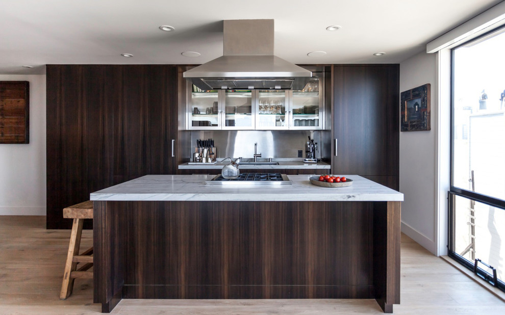 Cette image montre une cuisine parallèle design en bois foncé avec un placard à porte plane, une crédence métallisée, un sol en bois brun et îlot.