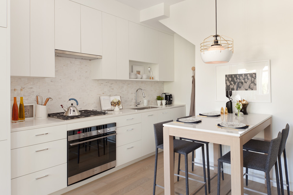 Bild på ett litet funkis linjärt kök och matrum, med en undermonterad diskho, släta luckor, vita skåp, vitt stänkskydd, rostfria vitvaror och bänkskiva i kvarts