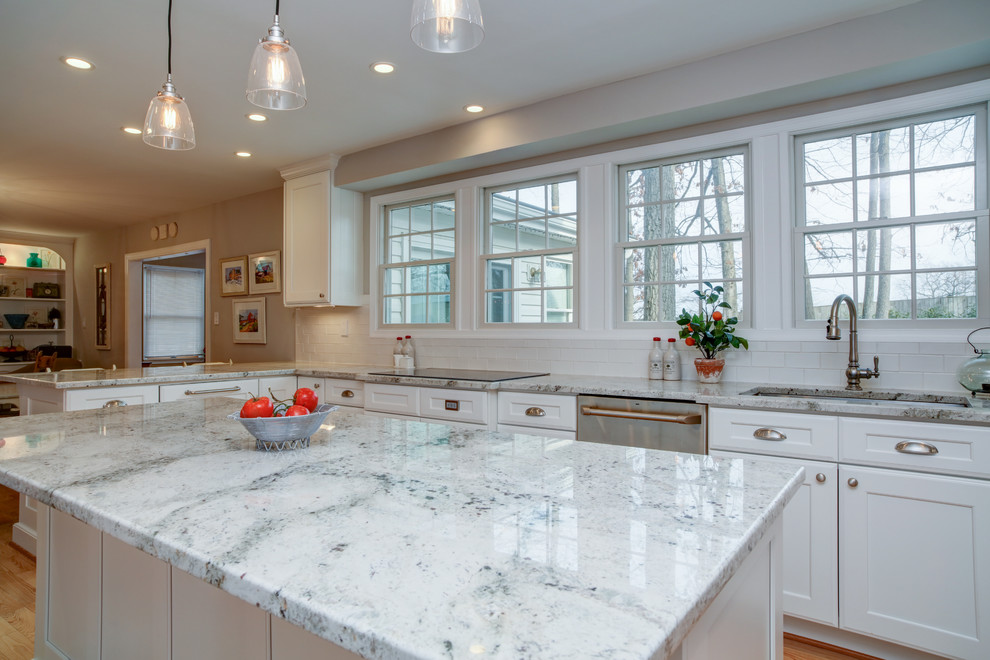 This is an example of a medium sized farmhouse u-shaped kitchen/diner in DC Metro with a single-bowl sink, shaker cabinets, white cabinets, engineered stone countertops, white splashback, metro tiled splashback, stainless steel appliances, light hardwood flooring and an island.