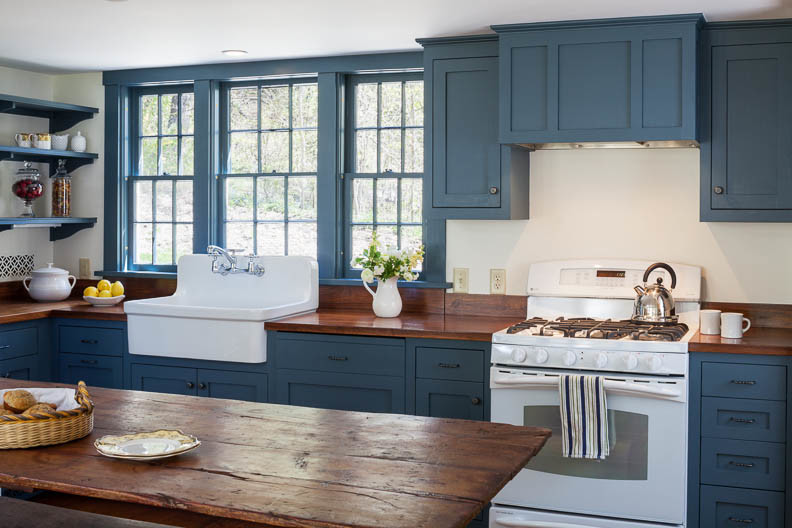 Mittelgroße Country Wohnküche in L-Form mit Landhausspüle, blauen Schränken, Arbeitsplatte aus Holz und weißen Elektrogeräten in Boston