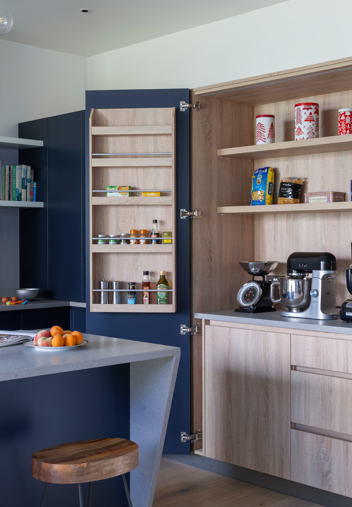Moderne Küche in L-Form mit flächenbündigen Schrankfronten, blauen Schränken, Küchenrückwand in Weiß, hellem Holzboden, Kücheninsel, beigem Boden und grauer Arbeitsplatte in London