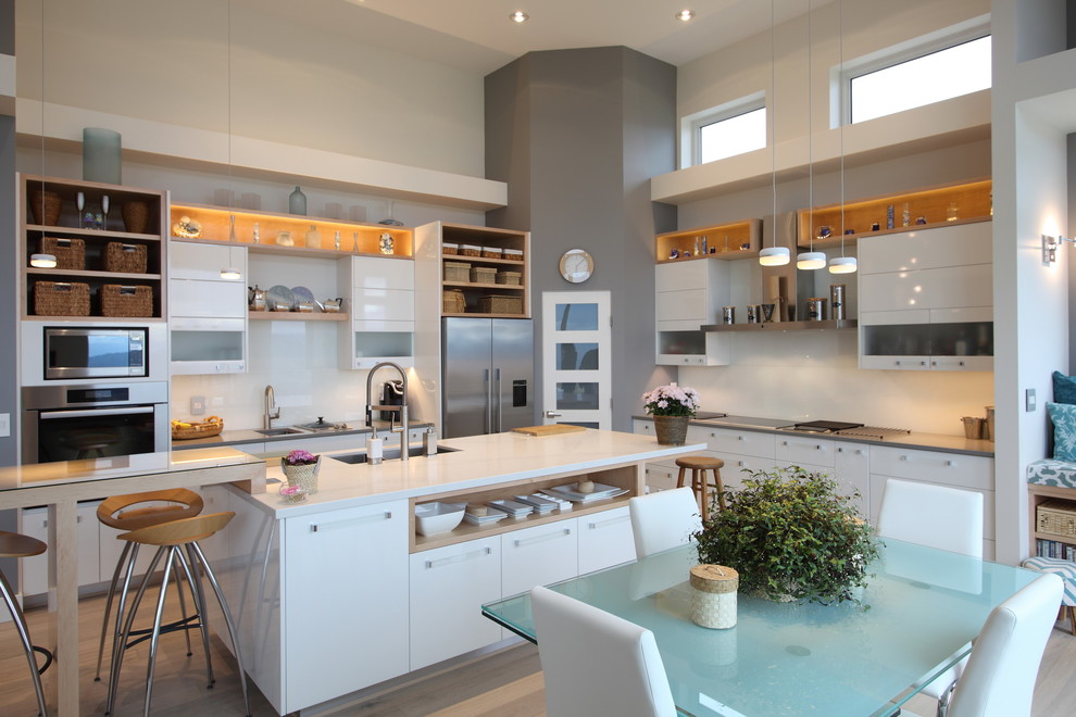 This is an example of a medium sized modern l-shaped open plan kitchen in Vancouver with a submerged sink, flat-panel cabinets, white cabinets, engineered stone countertops, white splashback, ceramic splashback, stainless steel appliances, light hardwood flooring and an island.