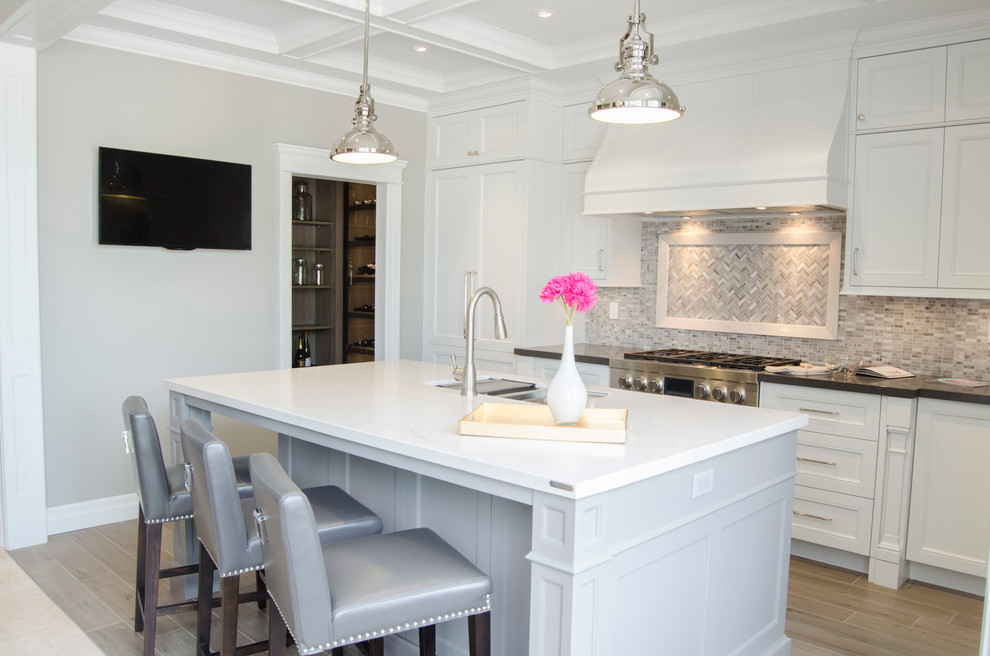 Eat-in kitchen - mid-sized traditional l-shaped ceramic tile eat-in kitchen idea in Toronto with an undermount sink, shaker cabinets, white cabinets, quartzite countertops, gray backsplash, stone tile backsplash, stainless steel appliances and an island