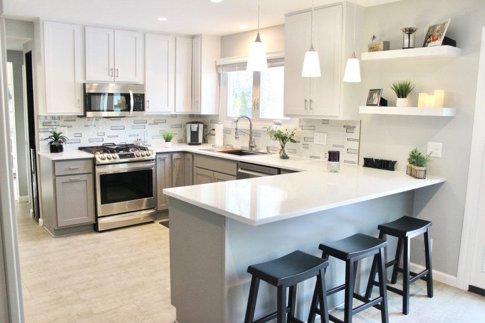 Example of a mid-sized transitional u-shaped ceramic tile and black floor eat-in kitchen design in Other with an undermount sink, flat-panel cabinets, gray cabinets, quartz countertops, gray backsplash, glass tile backsplash, stainless steel appliances, a peninsula and white countertops