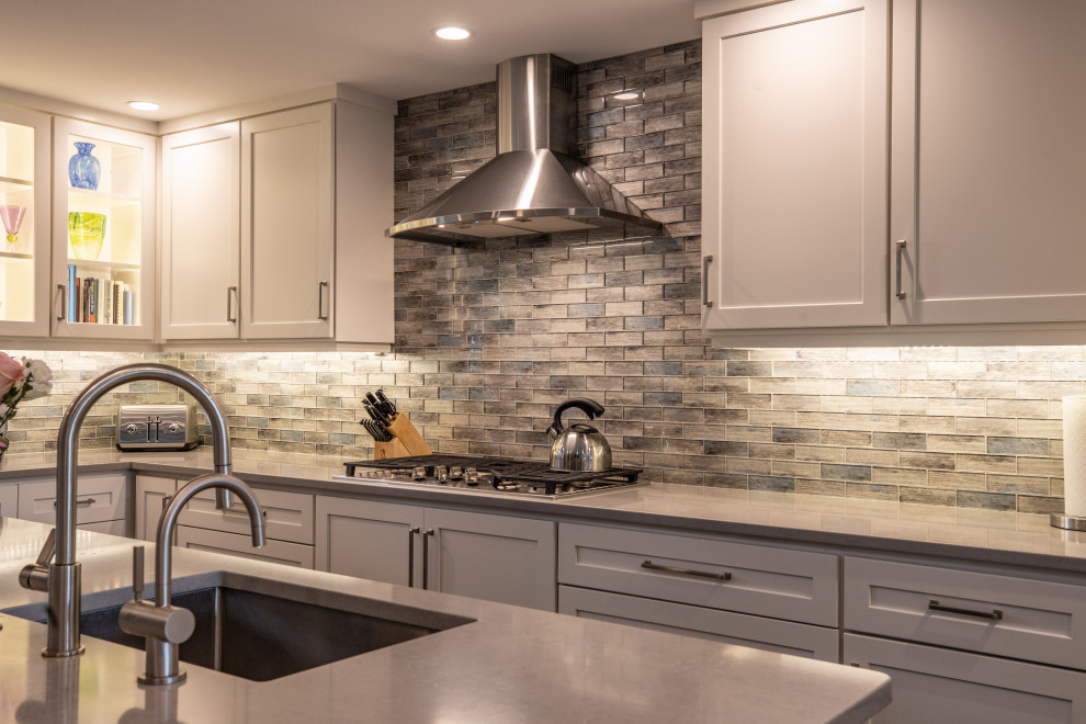 Mid-sized transitional l-shaped medium tone wood floor open concept kitchen photo in Philadelphia with an undermount sink, shaker cabinets, white cabinets, quartz countertops, multicolored backsplash, stainless steel appliances, an island and gray countertops