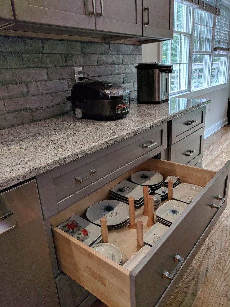 Inredning av ett modernt stort grå grått kök, med en rustik diskho, skåp i shakerstil, grå skåp, granitbänkskiva, grått stänkskydd, stänkskydd i stenkakel, rostfria vitvaror, ljust trägolv, en köksö och brunt golv