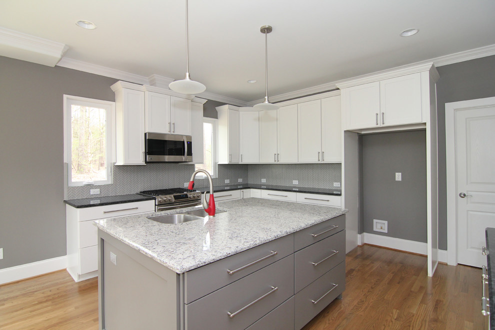 Example of a large trendy l-shaped light wood floor open concept kitchen design in Raleigh with a double-bowl sink, flat-panel cabinets, gray cabinets, granite countertops, gray backsplash, glass tile backsplash, stainless steel appliances and two islands