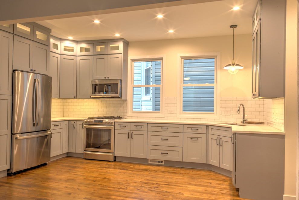 Modern inredning av ett mellanstort vit vitt kök, med en undermonterad diskho, skåp i shakerstil, grå skåp, bänkskiva i kvarts, vitt stänkskydd, stänkskydd i keramik, rostfria vitvaror, ljust trägolv och brunt golv