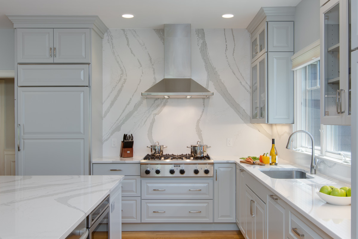 Example of a large transitional l-shaped medium tone wood floor open concept kitchen design in Boston with an undermount sink, raised-panel cabinets, gray cabinets, quartz countertops, stone slab backsplash, paneled appliances and an island