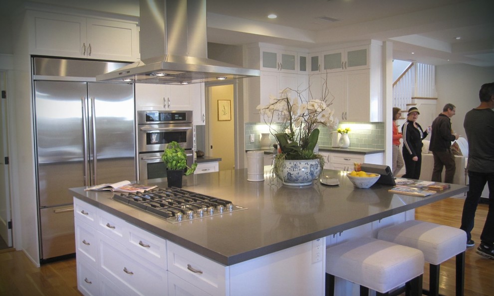 Inspiration for a large contemporary open plan kitchen in Los Angeles with shaker cabinets, white cabinets, engineered stone countertops, green splashback, glass tiled splashback, stainless steel appliances, light hardwood flooring and an island.
