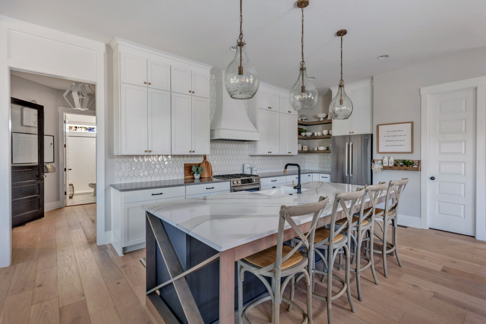 Example of a cottage l-shaped medium tone wood floor and brown floor kitchen design in Richmond with a farmhouse sink, shaker cabinets, white cabinets, white backsplash, stainless steel appliances, an island and gray countertops