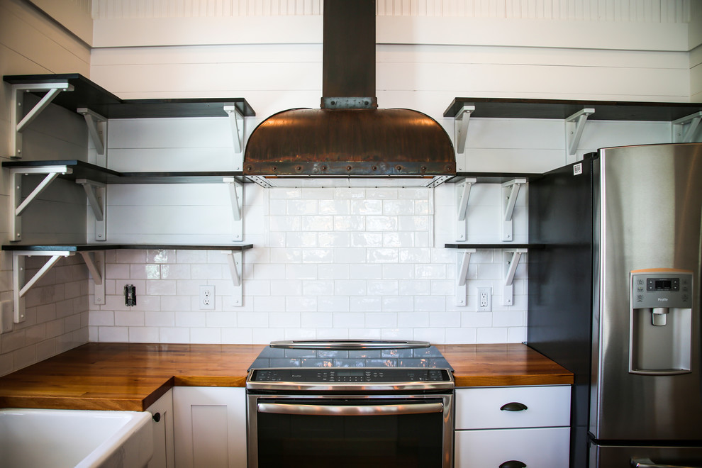 Foto på ett litet industriellt brun kök, med en rustik diskho, luckor med infälld panel, vita skåp, träbänkskiva, vitt stänkskydd, stänkskydd i tegel, rostfria vitvaror, plywoodgolv och brunt golv