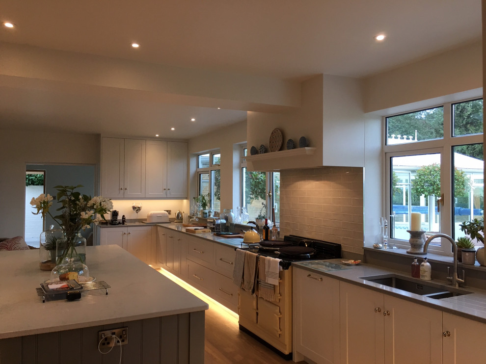 This is an example of a large rural u-shaped kitchen/diner in Devon with a submerged sink, shaker cabinets, white cabinets, quartz worktops, grey splashback, ceramic splashback, stainless steel appliances, vinyl flooring, an island, multi-coloured floors, grey worktops and exposed beams.
