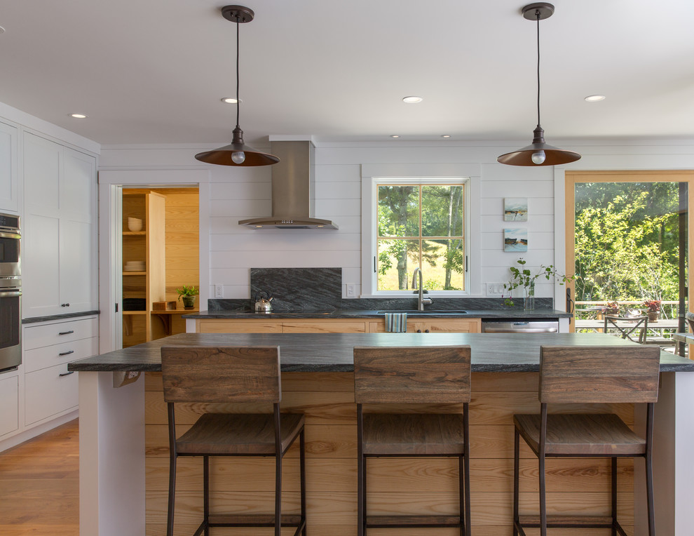 Example of a mid-sized transitional l-shaped light wood floor and brown floor open concept kitchen design in Portland Maine with granite countertops, gray backsplash, stone slab backsplash, stainless steel appliances, an island, white cabinets and an undermount sink