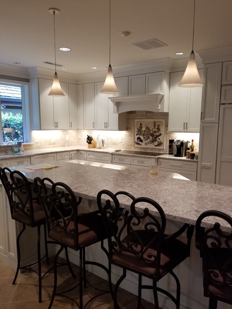 This is an example of a retro l-shaped kitchen/diner in DC Metro with a submerged sink, recessed-panel cabinets, white cabinets, engineered stone countertops, beige splashback, stone tiled splashback, integrated appliances, porcelain flooring, an island, brown floors and beige worktops.