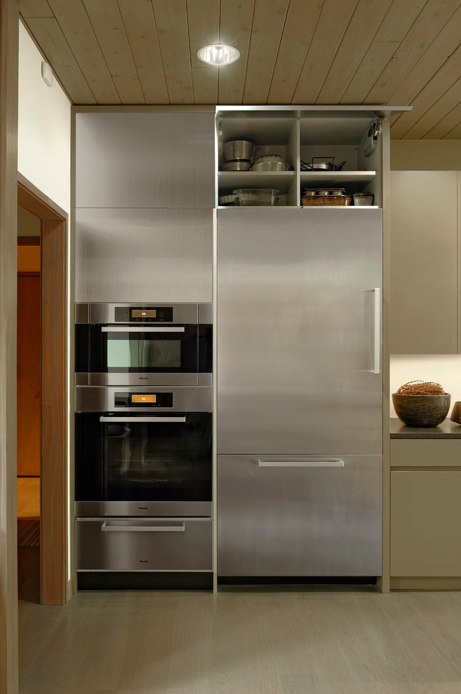 Ejemplo de cocina comedor actual, de tamaño medio, con armarios con paneles lisos, electrodomésticos de acero inoxidable, fregadero bajoencimera, puertas de armario de madera en tonos medios, suelo de madera oscura, una isla, encimera de acrílico y salpicadero blanco