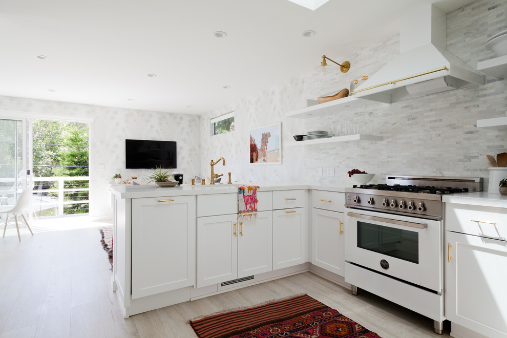 Design ideas for a medium sized nautical u-shaped open plan kitchen in Los Angeles with recessed-panel cabinets, white cabinets, marble worktops, white splashback, porcelain splashback, white appliances, light hardwood flooring and no island.