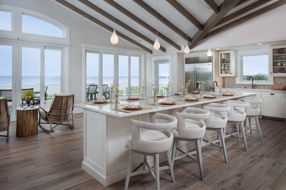 Inspiration for a large coastal l-shaped medium tone wood floor and brown floor open concept kitchen remodel in Other with white cabinets, quartzite countertops, multicolored backsplash, stainless steel appliances, an island, an undermount sink, mosaic tile backsplash and recessed-panel cabinets