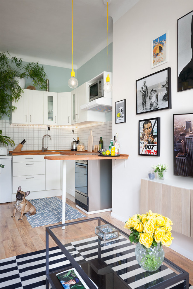 Foto på ett litet skandinaviskt kök, med en undermonterad diskho, skåp i shakerstil, vita skåp, träbänkskiva, vitt stänkskydd, stänkskydd i keramik, rostfria vitvaror, laminatgolv och en halv köksö
