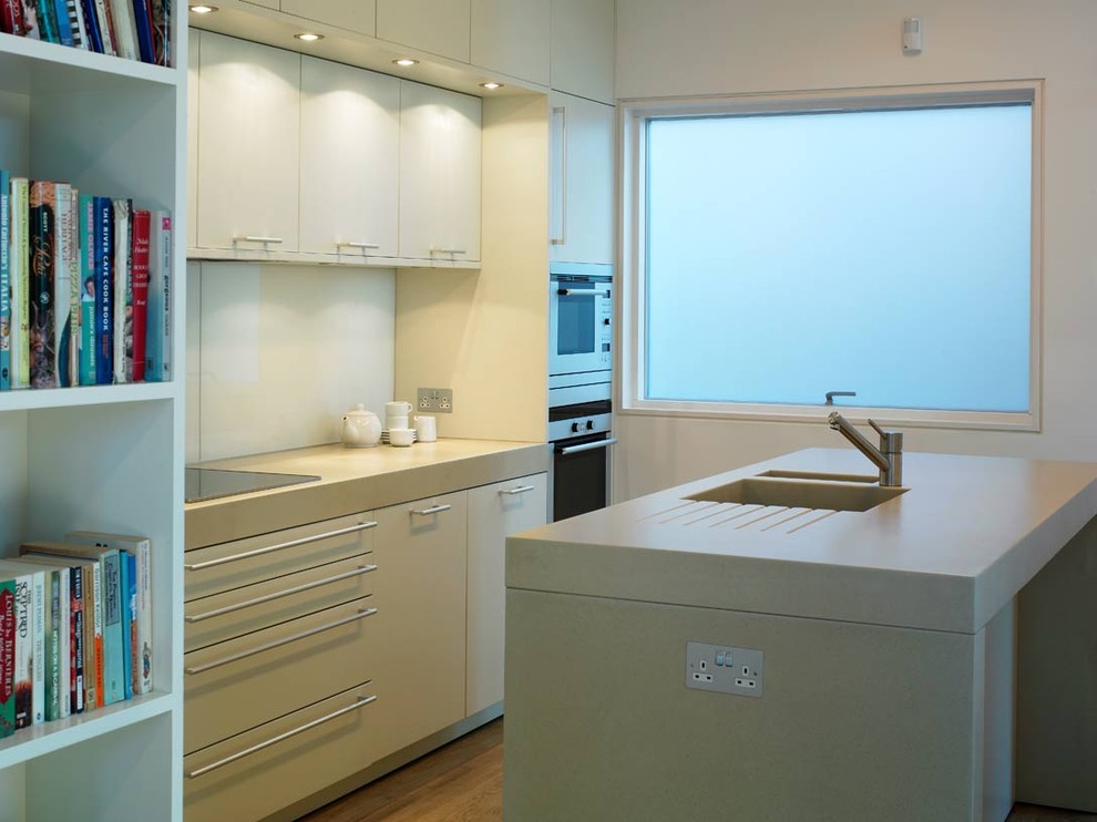 Idéer för ett modernt kök, med en integrerad diskho, släta luckor, vita skåp, vitt stänkskydd, glaspanel som stänkskydd och rostfria vitvaror