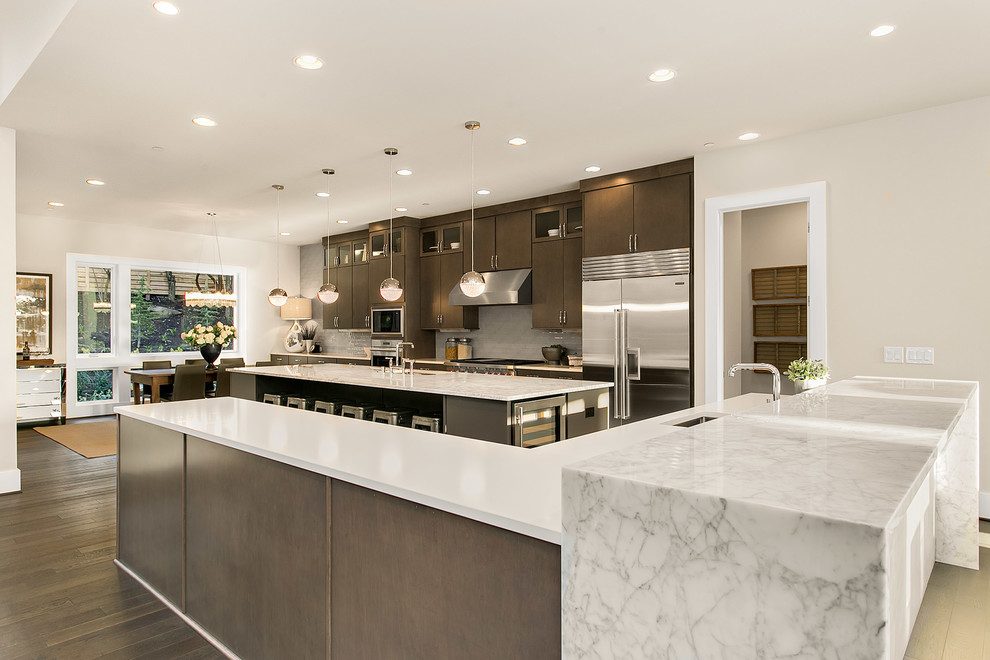 Expansive modern kitchen in Seattle with a built-in sink, flat-panel cabinets, medium wood cabinets, engineered stone countertops, grey splashback, glass tiled splashback, stainless steel appliances, medium hardwood flooring and multiple islands.