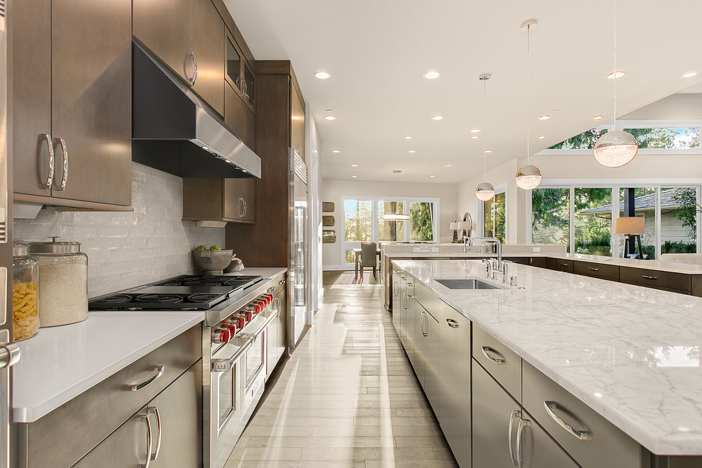 Photo of an expansive modern kitchen in Seattle with a built-in sink, flat-panel cabinets, medium wood cabinets, engineered stone countertops, grey splashback, glass tiled splashback, stainless steel appliances, medium hardwood flooring and multiple islands.