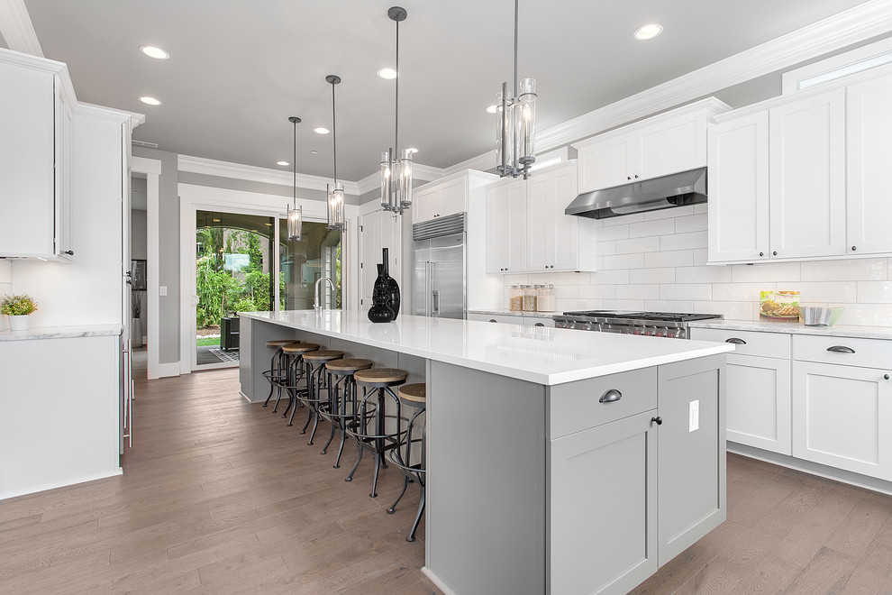 Inspiration for a large traditional l-shaped kitchen/diner in Seattle with shaker cabinets, white cabinets, engineered stone countertops, white splashback, stainless steel appliances, medium hardwood flooring and an island.