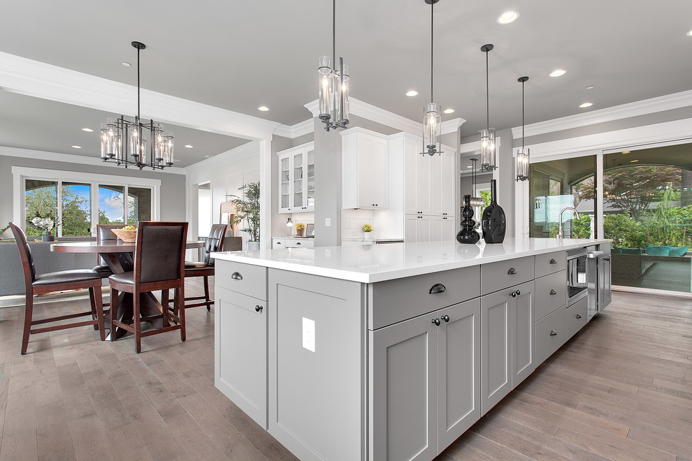 Large classic l-shaped kitchen/diner in Seattle with shaker cabinets, white cabinets, engineered stone countertops, white splashback, stainless steel appliances, medium hardwood flooring and an island.
