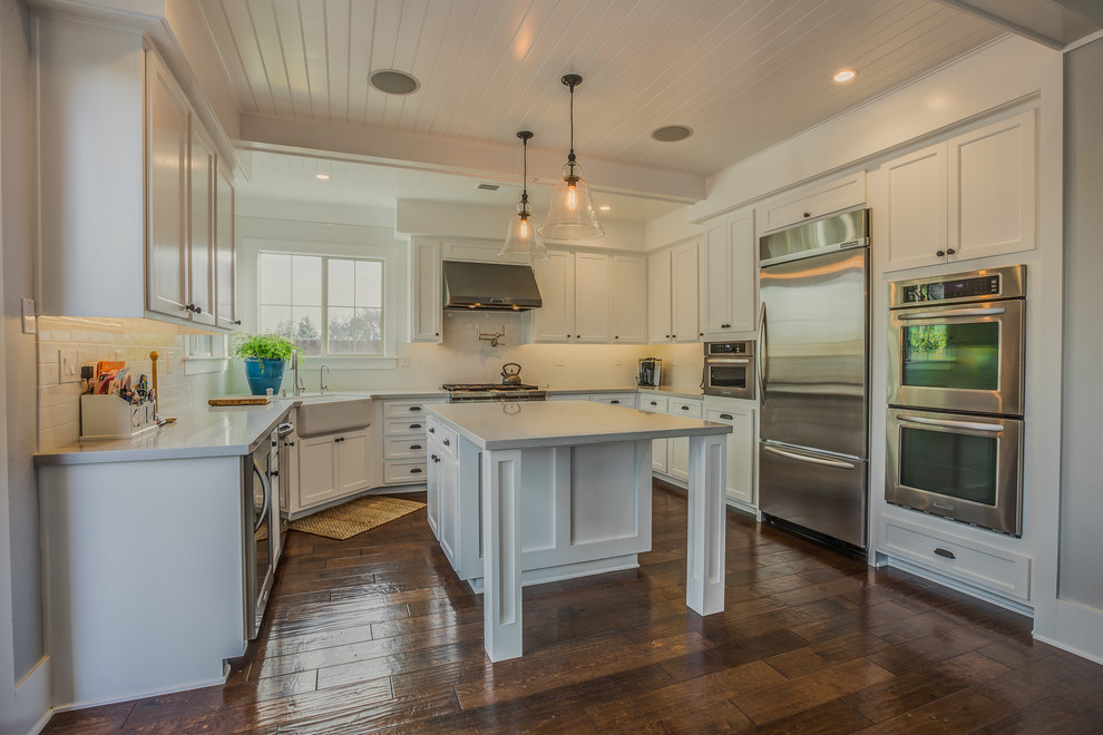 This is an example of a nautical u-shaped kitchen/diner in San Diego with a belfast sink, shaker cabinets, white cabinets, engineered stone countertops, white splashback, metro tiled splashback and stainless steel appliances.