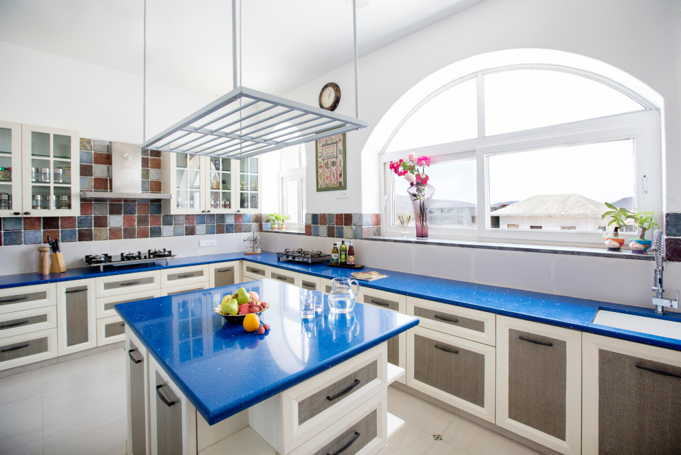 Aménagement d'une cuisine méditerranéenne en L avec un évier encastré, un placard avec porte à panneau encastré, une crédence multicolore, îlot, un sol gris et un plan de travail bleu.
