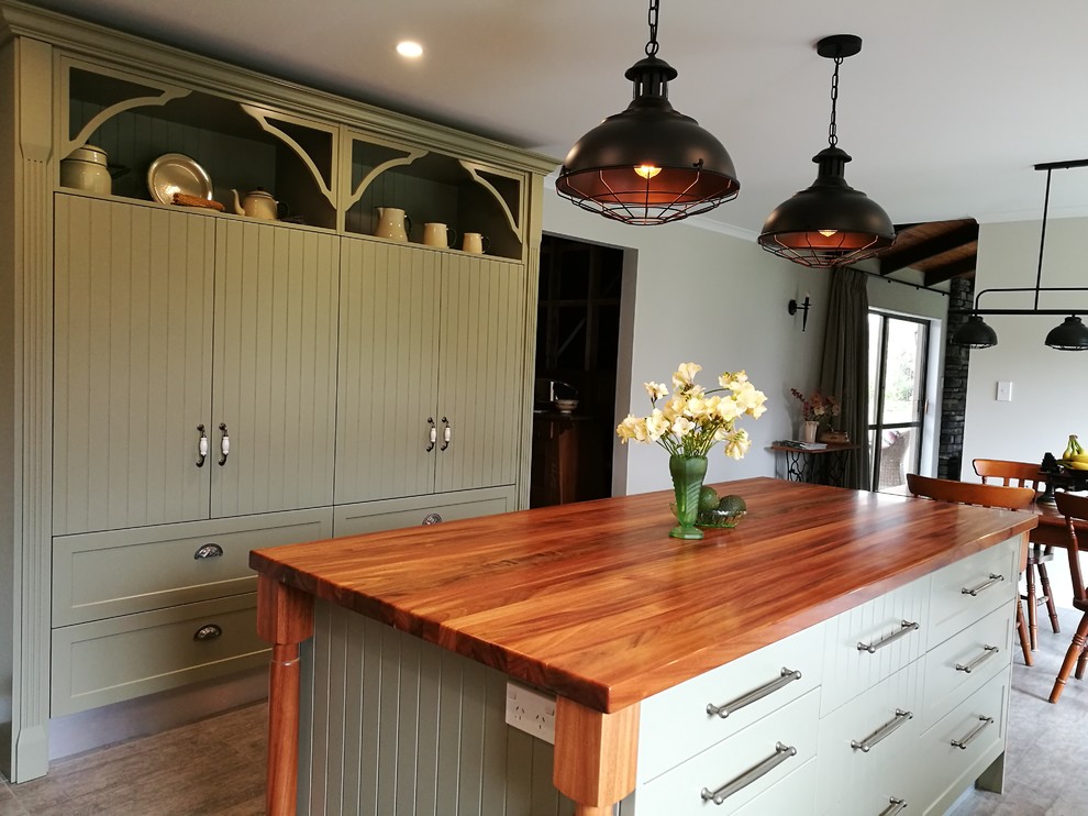 Photo of a large rural u-shaped kitchen in Wellington with an integrated sink, shaker cabinets, white cabinets, wood worktops, green splashback, metro tiled splashback, stainless steel appliances, terracotta flooring, an island, grey floors and brown worktops.