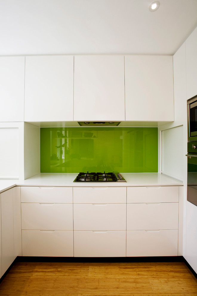 Modern kitchen in Sydney with engineered stone countertops, green splashback and glass sheet splashback.