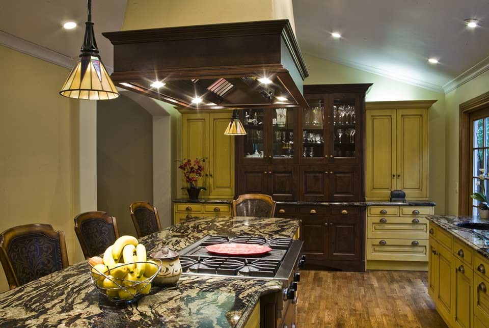 Foto på ett mellanstort amerikanskt kök och matrum, med en undermonterad diskho, luckor med upphöjd panel, gula skåp, granitbänkskiva, rostfria vitvaror, mellanmörkt trägolv och flera köksöar