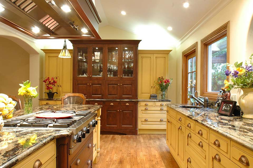 Inspiration for a mid-sized craftsman medium tone wood floor eat-in kitchen remodel in San Francisco with an undermount sink, raised-panel cabinets, yellow cabinets, granite countertops, stainless steel appliances and two islands