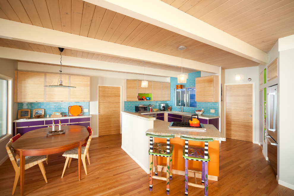 This is an example of a medium sized eclectic u-shaped kitchen/diner in San Luis Obispo with flat-panel cabinets, light wood cabinets, metro tiled splashback, stainless steel appliances, a submerged sink, blue splashback, medium hardwood flooring, a breakfast bar, brown floors, recycled glass countertops and multicoloured worktops.