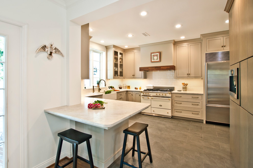 Example of a mid-sized transitional u-shaped porcelain tile and gray floor enclosed kitchen design in Nashville with a farmhouse sink, shaker cabinets, beige cabinets, marble countertops, white backsplash, porcelain backsplash, stainless steel appliances, no island and multicolored countertops