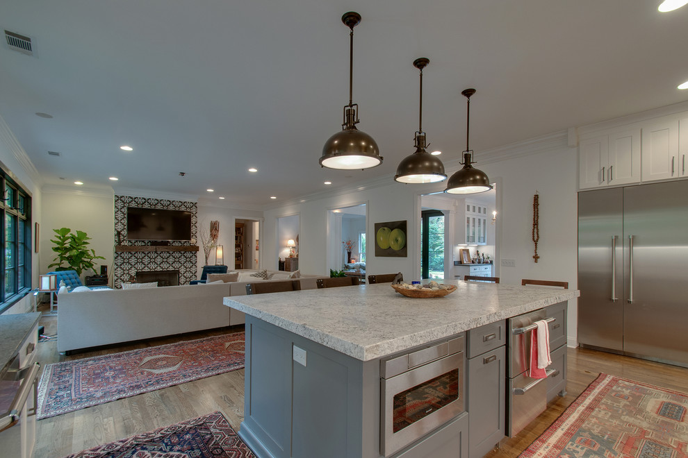 This is an example of a medium sized romantic open plan kitchen in Nashville with a submerged sink, shaker cabinets, white cabinets, granite worktops, white splashback, ceramic splashback, stainless steel appliances, medium hardwood flooring, an island, brown floors, grey worktops and feature lighting.