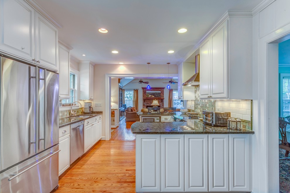 Exempel på ett mellanstort klassiskt kök, med en undermonterad diskho, luckor med upphöjd panel, vita skåp, granitbänkskiva, flerfärgad stänkskydd, stänkskydd i glaskakel, rostfria vitvaror, mellanmörkt trägolv och en halv köksö
