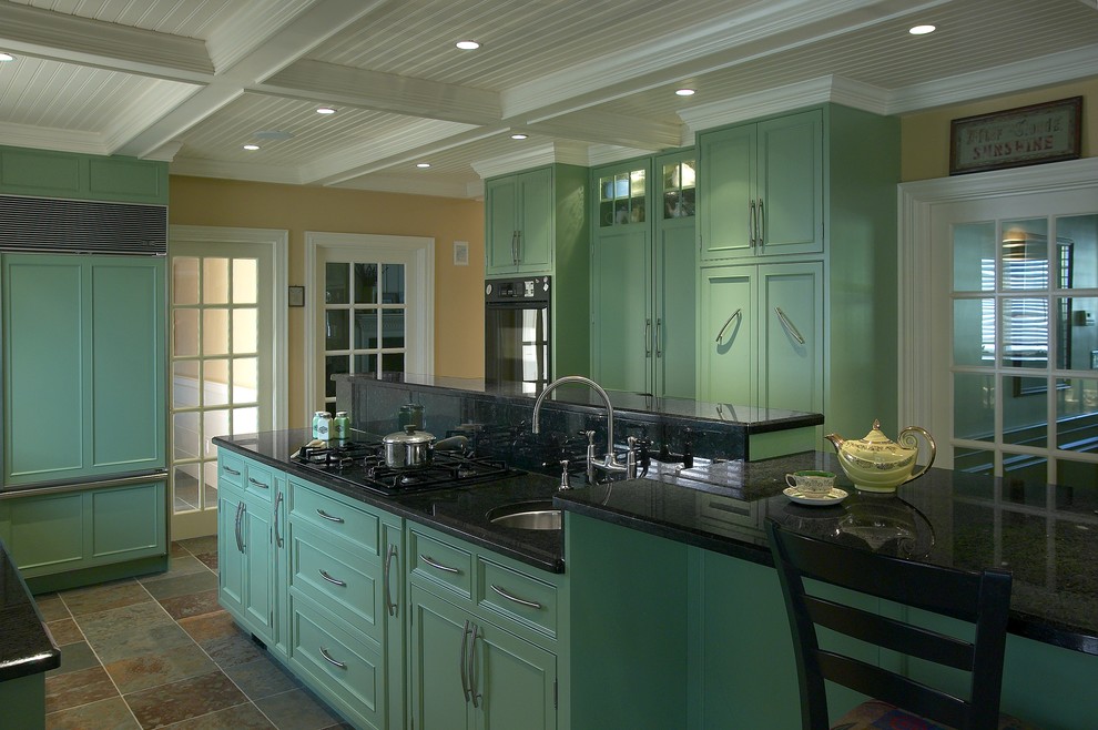 Eklektisk inredning av ett stort kök, med en rustik diskho, luckor med infälld panel, gröna skåp, granitbänkskiva, svarta vitvaror, skiffergolv och en köksö