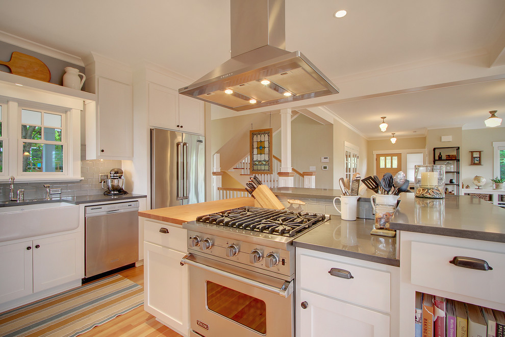 Foto på ett mellanstort amerikanskt kök, med rostfria vitvaror, en rustik diskho, luckor med infälld panel, vita skåp, grått stänkskydd, stänkskydd i tunnelbanekakel, ljust trägolv och en köksö