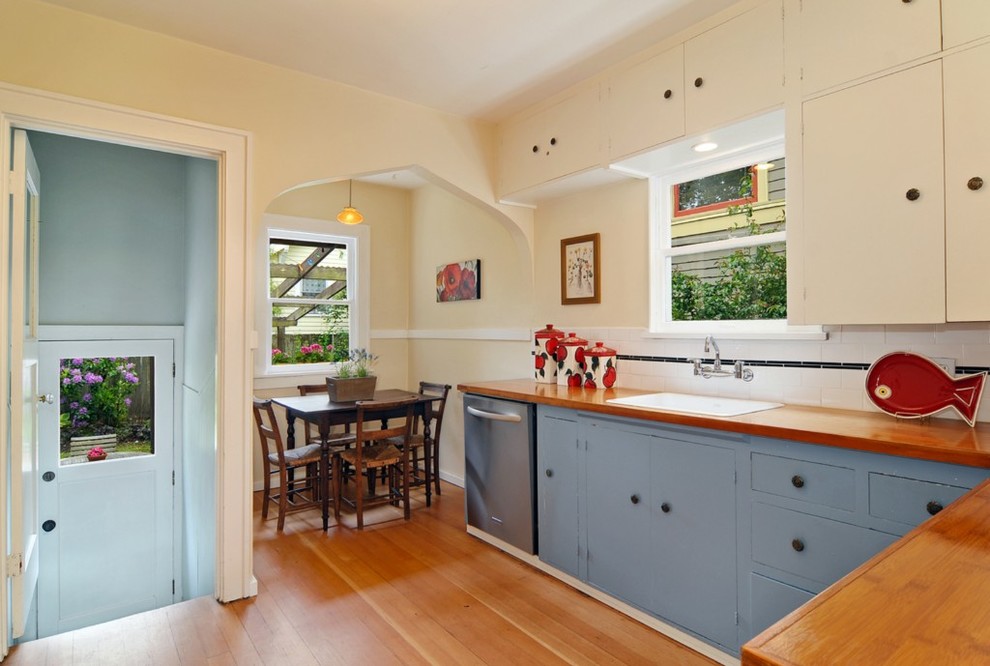 Arts and crafts eat-in kitchen photo in Seattle with a drop-in sink, flat-panel cabinets, blue cabinets, wood countertops, white backsplash, ceramic backsplash and stainless steel appliances